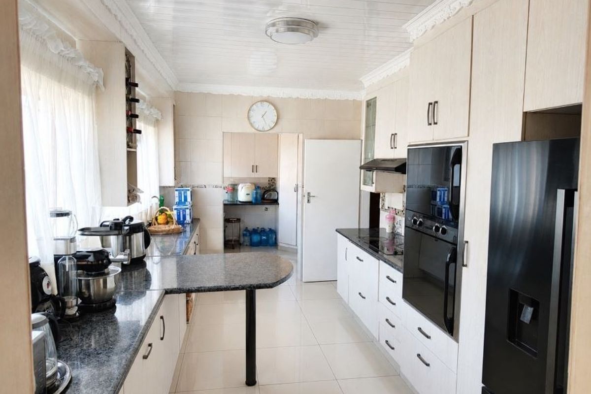A functional kitchen featuring granite countertops, built-in cabinetry, integrated oven, and a breakfast bar, with tiled flooring and a clean, neutral aesthetic.