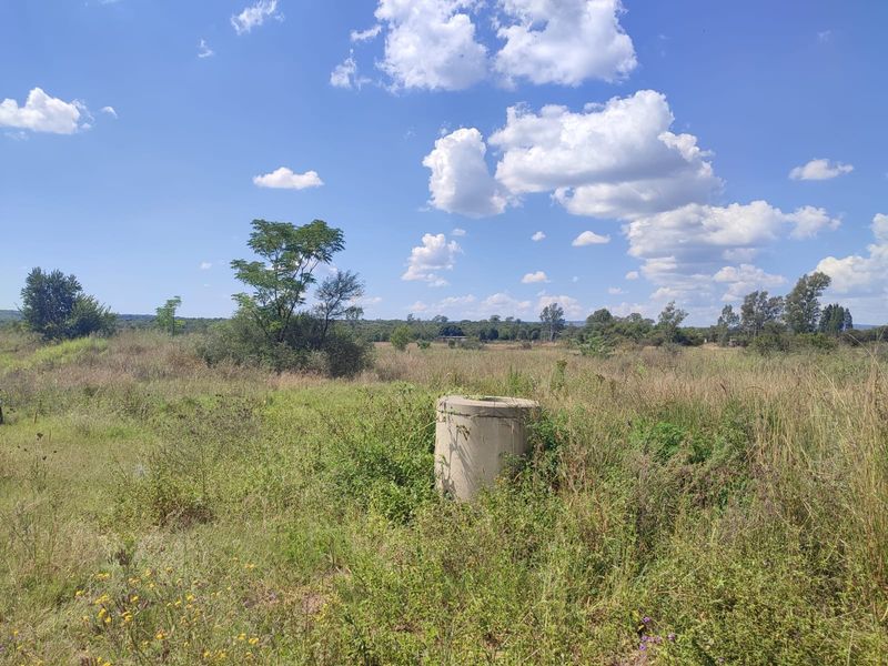 An expansive open field on the farm property featuring a concrete well casing surrounded by natural vegetation and native grasses.