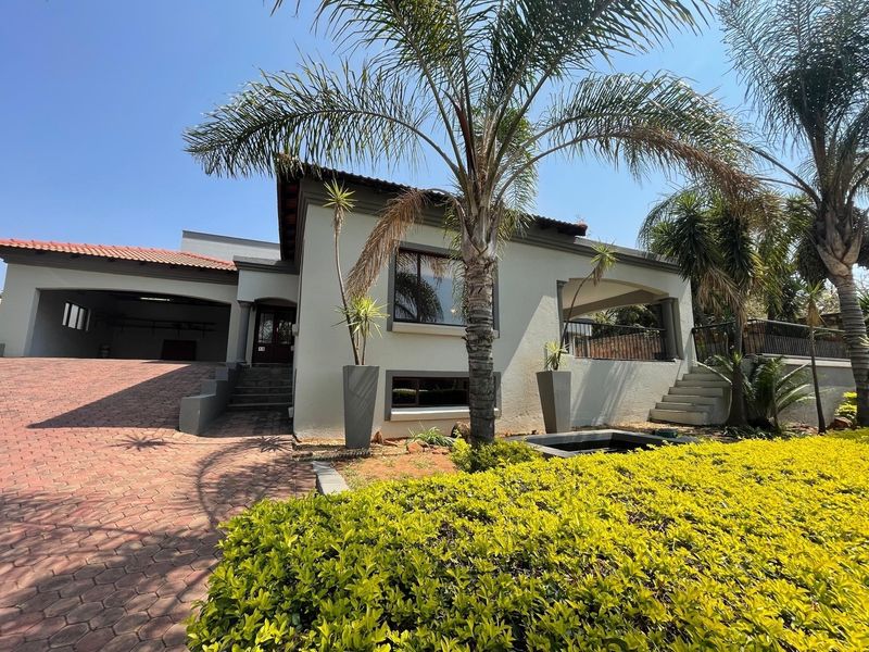 Front elevation of a residential property featuring a paved driveway, double garage, covered patio, and well-maintained landscaped garden.