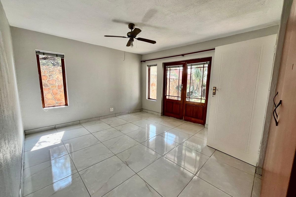 An empty living room featuring light-colored tiled flooring, a ceiling fan, and wooden framed glass doors providing access to the exterior.