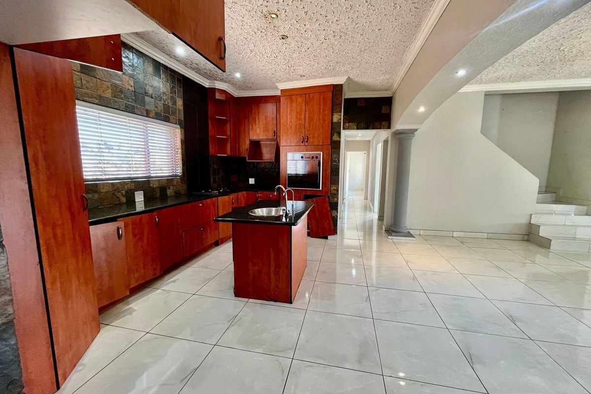 Spacious kitchen featuring dark wood cabinetry, granite countertops, a central island with a sink, and tiled flooring, opening into an adjacent living area.