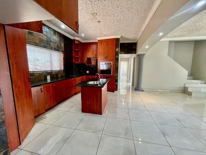 Spacious kitchen featuring dark wood cabinetry, granite countertops, a central island with a sink, and tiled flooring, opening into an adjacent living area.