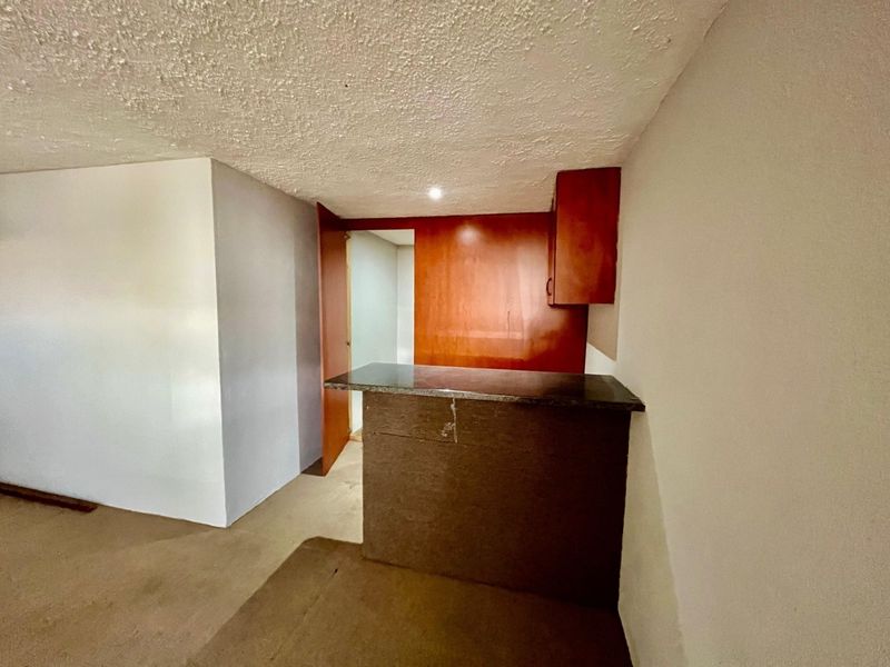 A compact kitchen area featuring built-in cabinetry and a stone-topped breakfast bar, currently vacant and awaiting modernization.