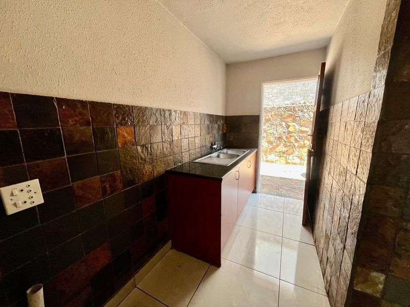 A functional scullery or utility area featuring built-in cabinetry, a stainless steel sink, and stone tile wall finishes with direct access to the exterior.