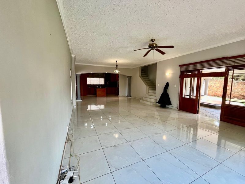 Spacious open-plan living area featuring large floor tiles, a ceiling fan, and a staircase, leading into a recessed kitchen space with direct patio access.