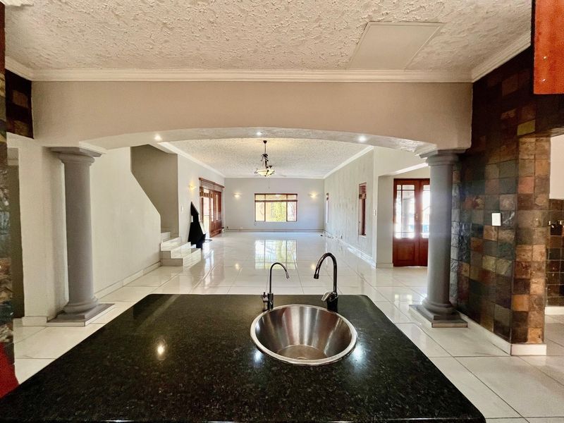 Spacious open-plan living area featuring a granite kitchen island with sink, decorative columns, and an archway leading to a bright, tiled living space.