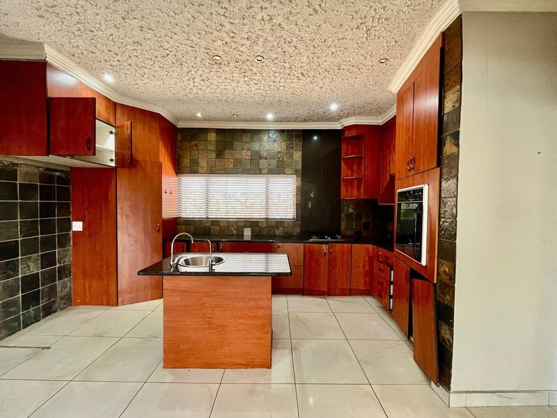 A spacious kitchen featuring dark wood cabinetry, granite countertops, a central island with a sink, and stone tile accents.
