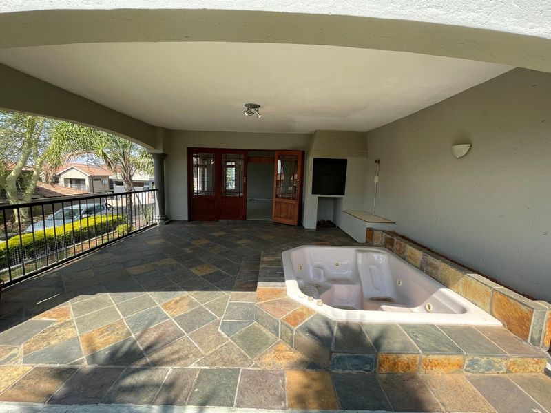 Covered balcony featuring a built-in jacuzzi, stone tile flooring, and a built-in braai area, offering a functional outdoor entertainment space.