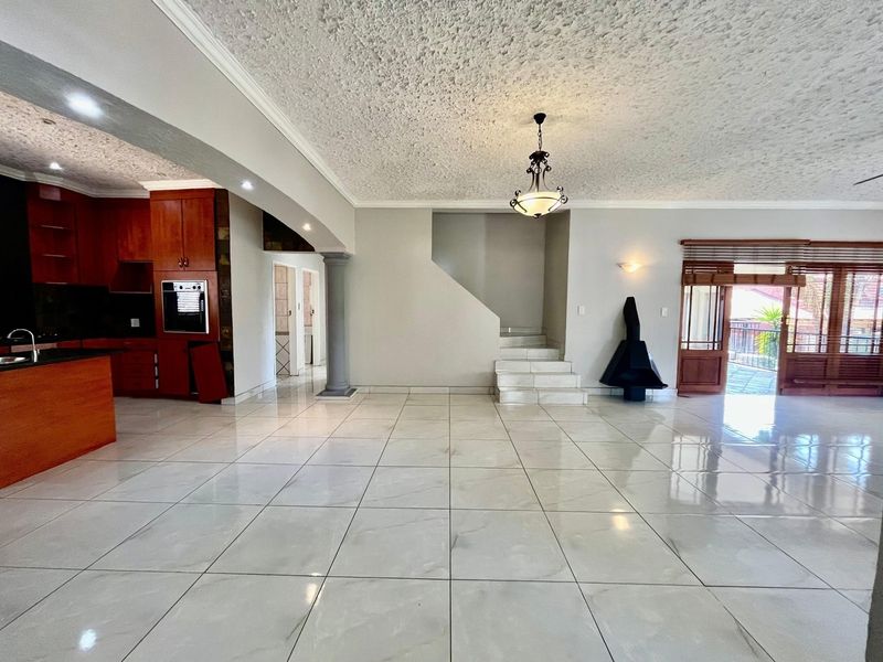 Spacious open-plan living area featuring large format floor tiles, a built-in kitchen, a feature staircase, and a fireplace with access to an outdoor patio.