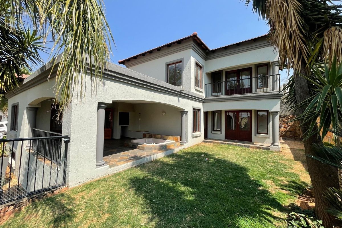 Rear view of a two-story house featuring a covered patio with a built-in jacuzzi, upper-level balcony, and a well-maintained garden area.