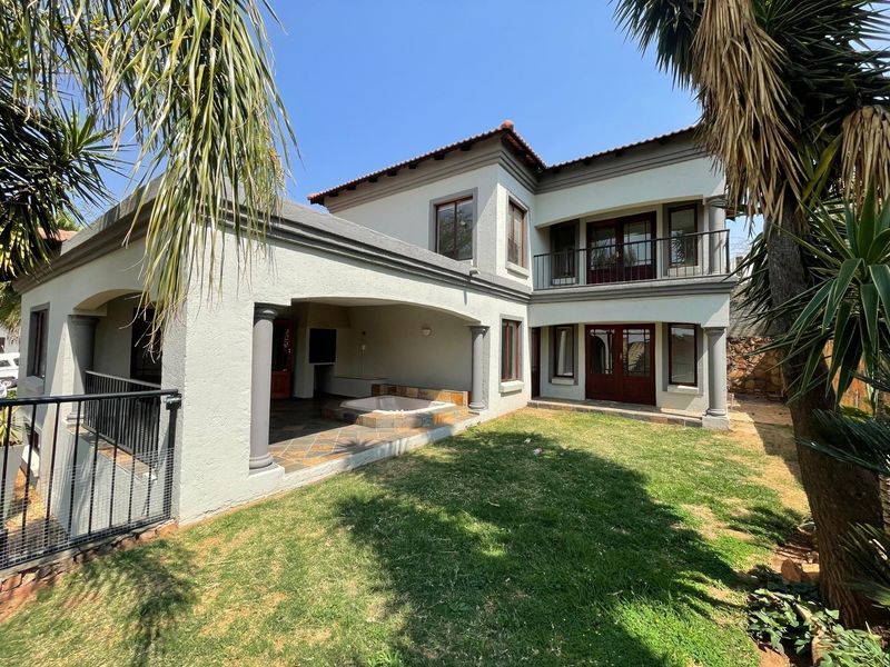 Rear view of a two-story house featuring a covered patio with a built-in jacuzzi, upper-level balcony, and a well-maintained garden area.