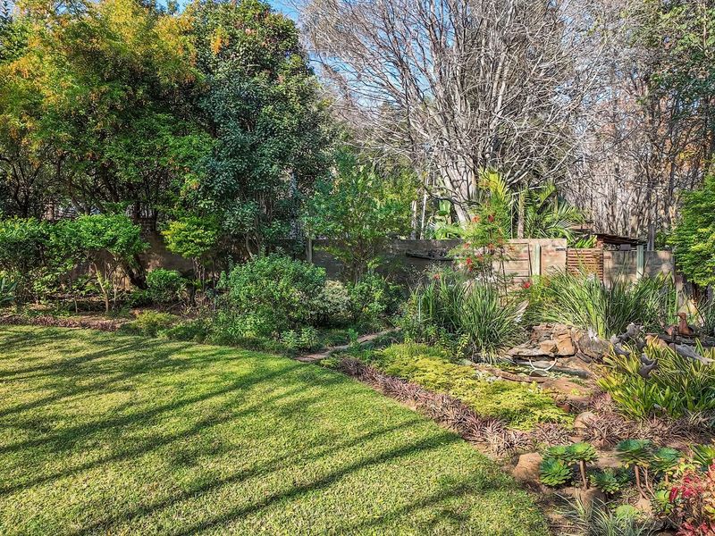 A lush, well-maintained garden featuring a stone water feature, mature trees, and established landscaping with a boundary wall.