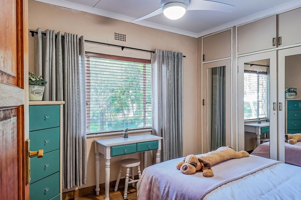 A bedroom featuring built-in cupboards with mirrored panels, a ceiling fan, and a window with venetian blinds.