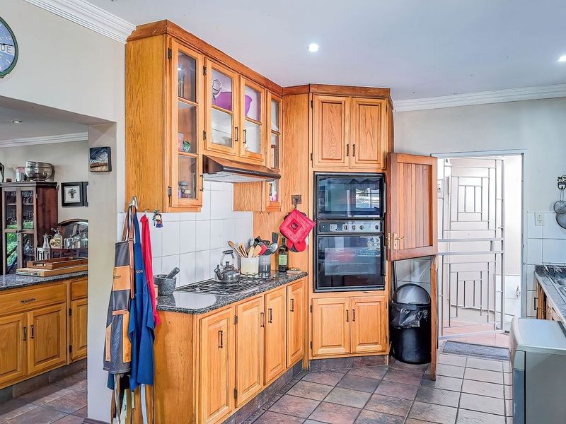 A functional kitchen featuring wooden cabinetry, granite countertops, a built-in double oven, and tiled flooring, with direct access to an exterior security gate.
