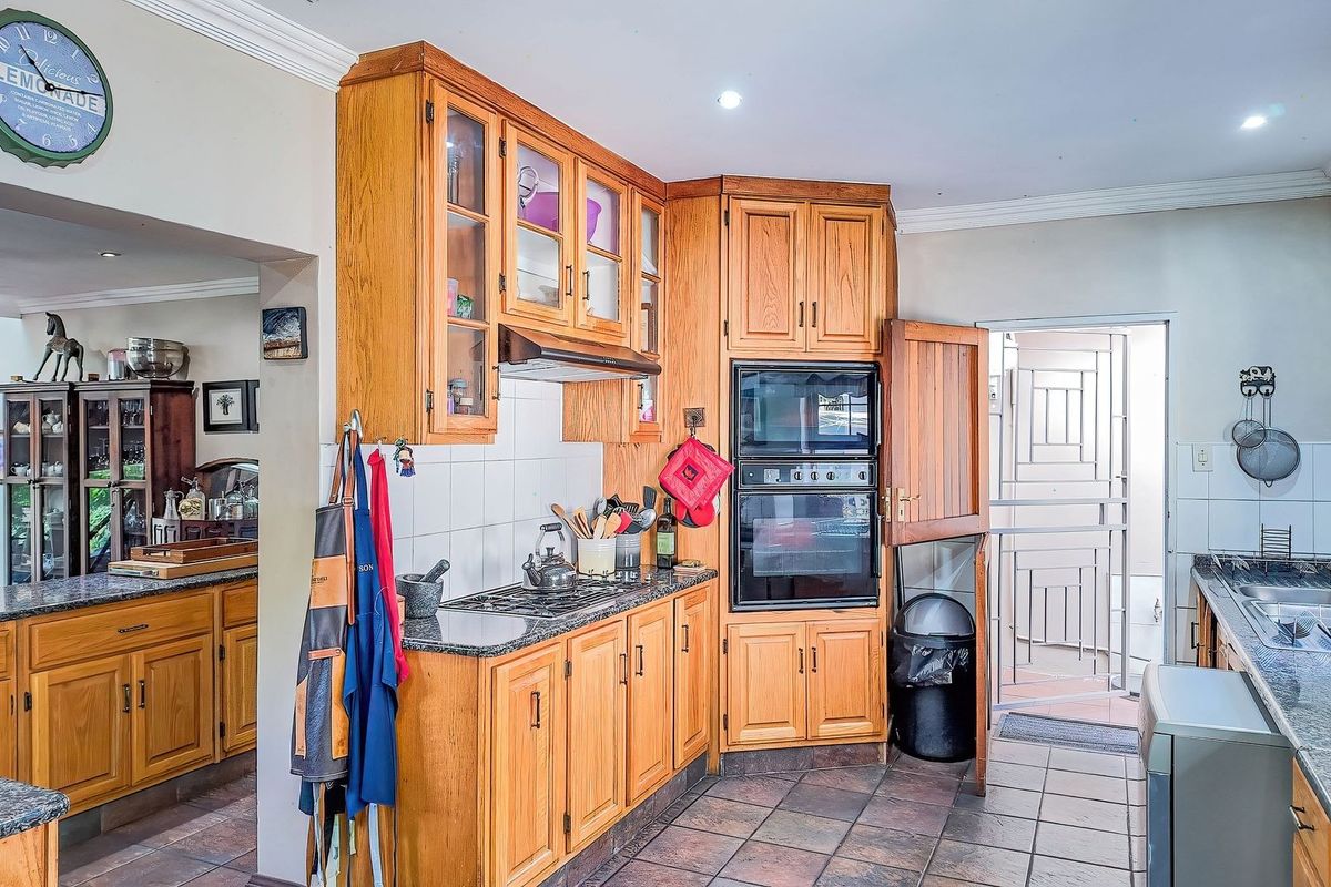 A functional kitchen featuring wooden cabinetry, granite countertops, a built-in double oven, and tiled flooring, with direct access to an exterior security gate.