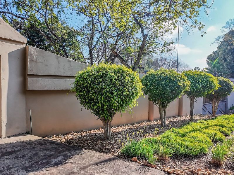 A well-maintained front entrance featuring a solid boundary wall, pedestrian gate, and neatly landscaped garden beds along the paved driveway.