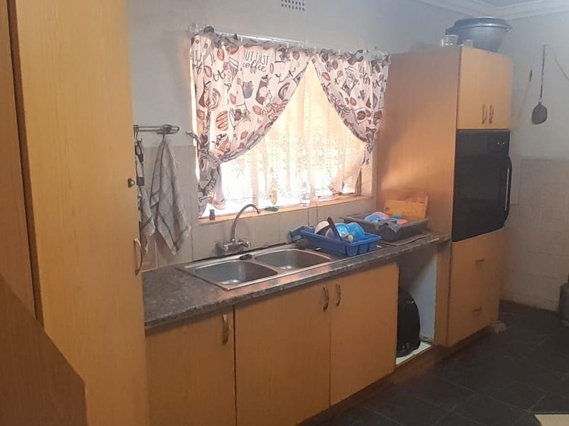 A dated kitchen featuring wood-look cabinetry, laminate countertops, a double basin sink, and a built-in oven, offering potential for a modern renovation.
