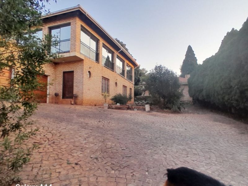 A view of the front exterior of a brick house featuring a paved driveway, balcony with metal railings, and integrated garage.