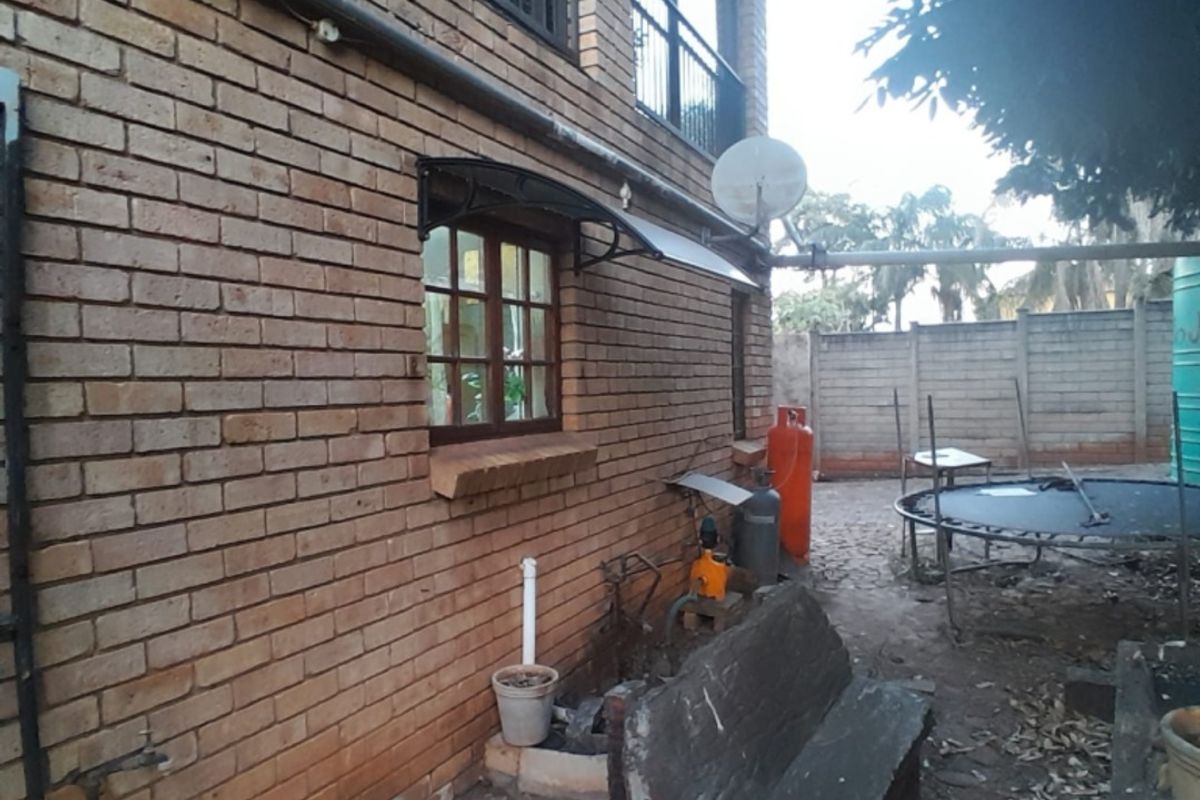Rear exterior view of a face brick house featuring a balcony with metal railings and a window awning.
