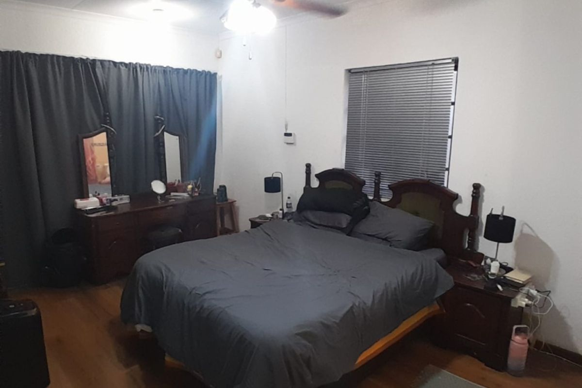 A functional bedroom featuring laminate flooring, a ceiling fan, and venetian blinds, providing a comfortable and well-lit sleeping space.