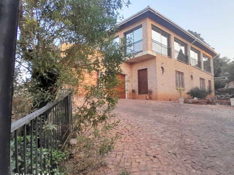 A two-story brick house featuring a paved driveway, integrated garage, and upper-level balcony with large windows.