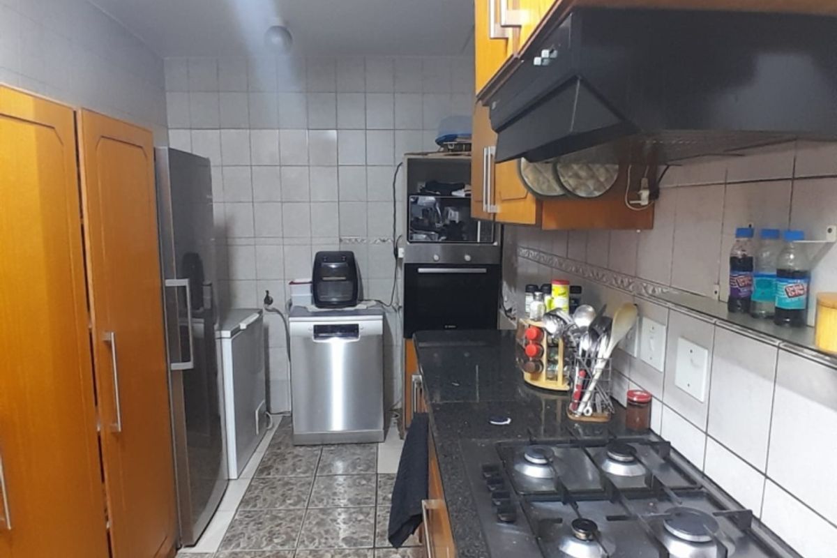 A functional kitchen featuring dark granite countertops, a gas hob with extractor fan, built-in oven, and ample wooden cabinetry with tiled finishes.