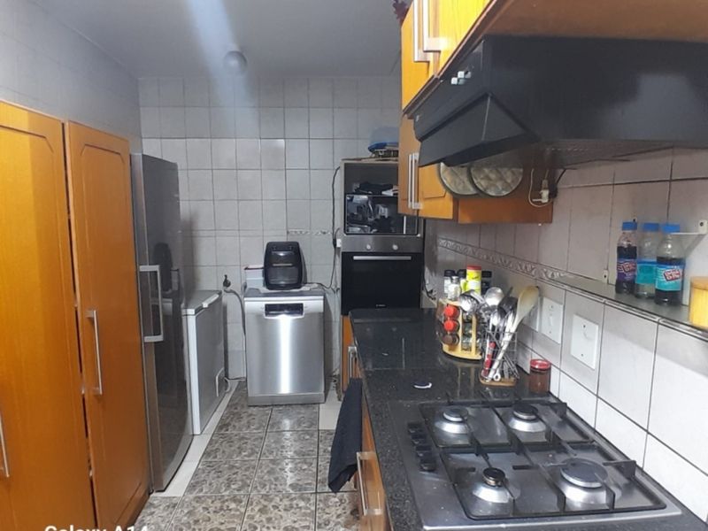 A functional kitchen featuring dark granite countertops, a gas hob with extractor fan, built-in oven, and ample wooden cabinetry with tiled finishes.