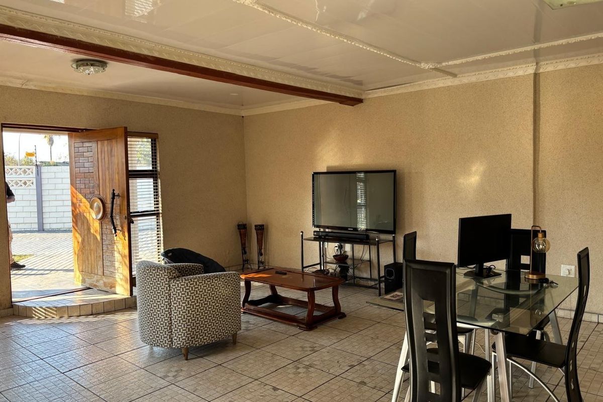 A living room area featuring tiled flooring, decorative ceiling molding, and a wooden entrance door leading to the exterior.
