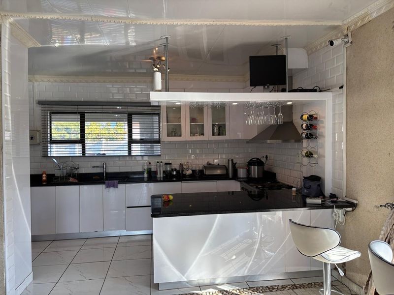 A modern kitchen featuring white cabinetry, black granite countertops, a breakfast bar, and a subway tile backsplash with integrated extractor fan.