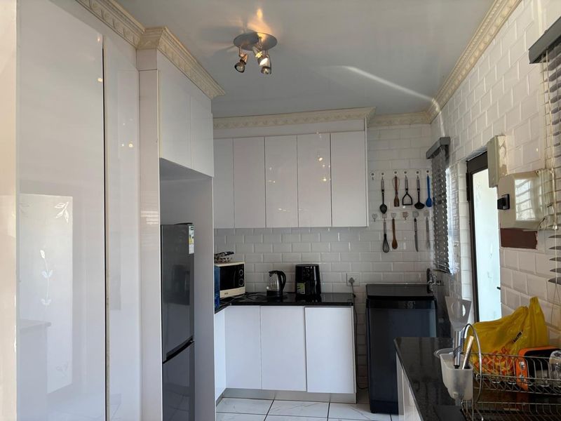 A modern kitchen featuring white gloss cabinetry, subway tile backsplash, black granite countertops, and tiled flooring with decorative ceiling coving.
