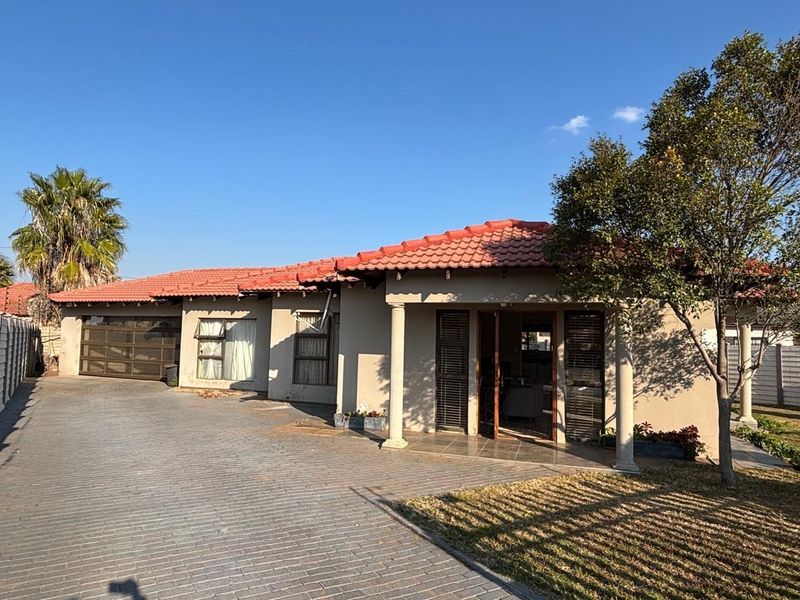 Front elevation of a single-story house featuring a tiled roof, paved driveway, integrated garage, and a covered entrance porch with structural columns.