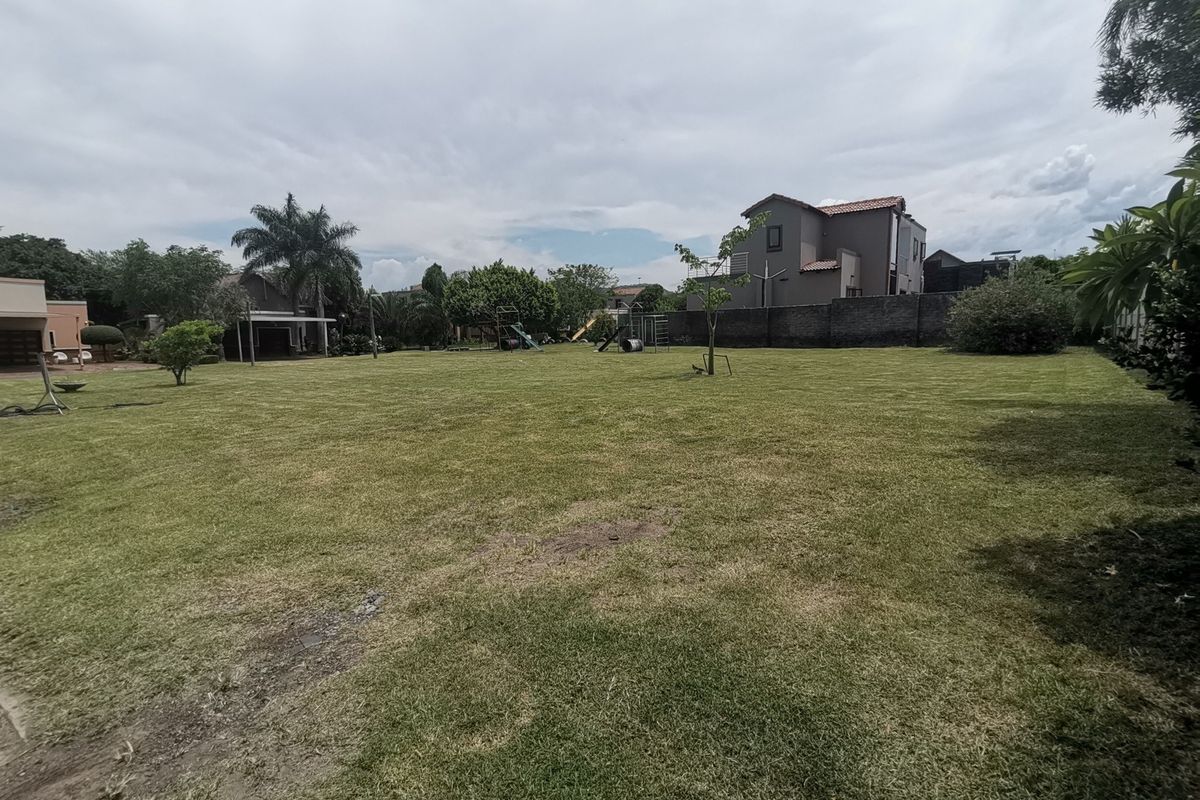 A spacious, well-maintained residential garden featuring a large lawn area, perimeter boundary walls, and established trees.