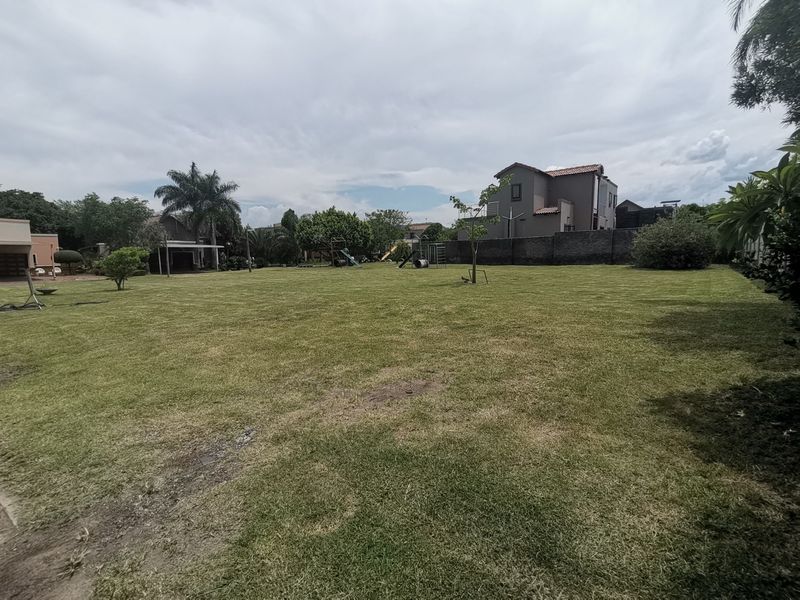 A spacious, well-maintained residential garden featuring a large lawn area, perimeter boundary walls, and established trees.