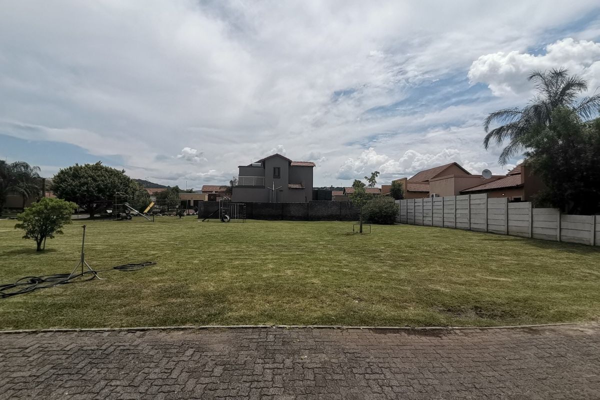 A spacious, well-maintained residential garden featuring a large lawn, paved driveway access, and perimeter precast concrete walling.