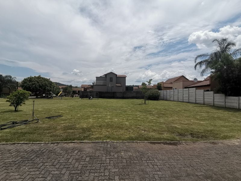 A spacious, well-maintained residential garden featuring a large lawn, paved driveway access, and perimeter precast concrete walling.