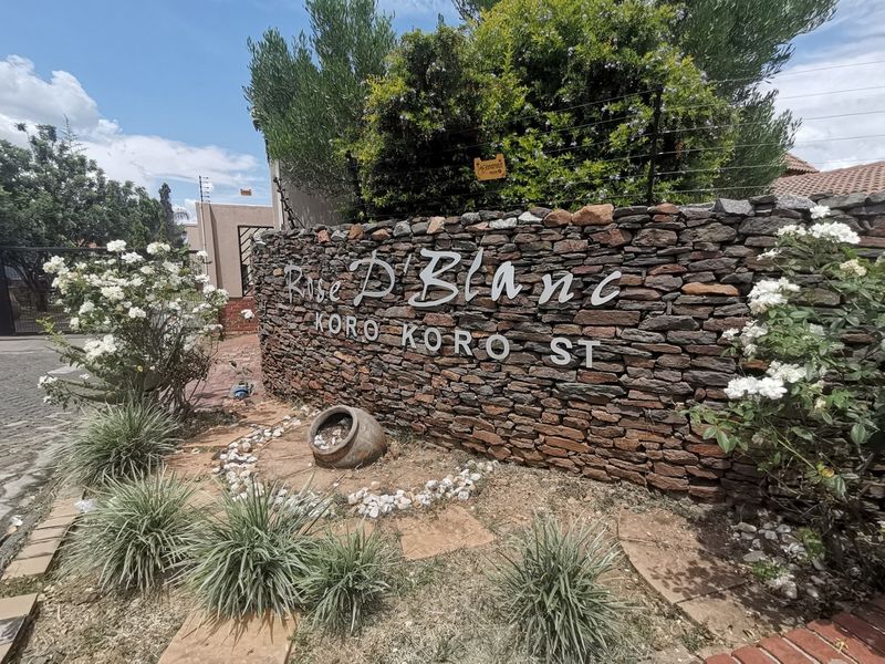 Front entrance signage wall for Rose D'Blanc estate featuring stone cladding, electric fencing, and established garden landscaping.