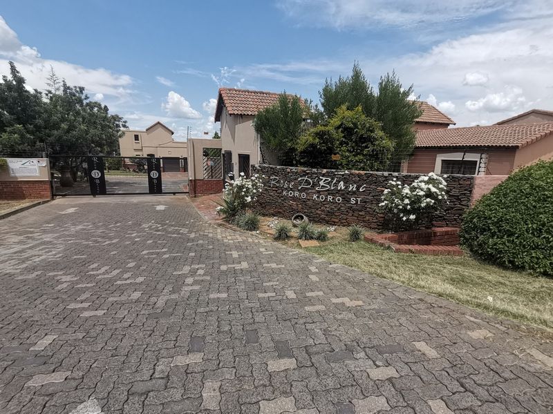 Entrance view of Rose D'Blanc residential estate featuring a paved driveway, stone signage wall, and secure gated access.