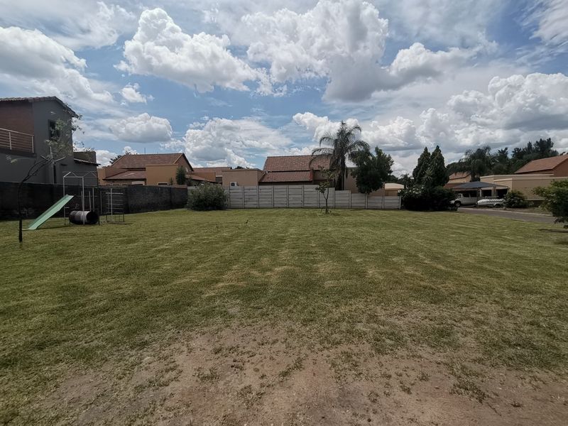A spacious, well-maintained residential garden featuring a large lawn area enclosed by perimeter boundary walls.