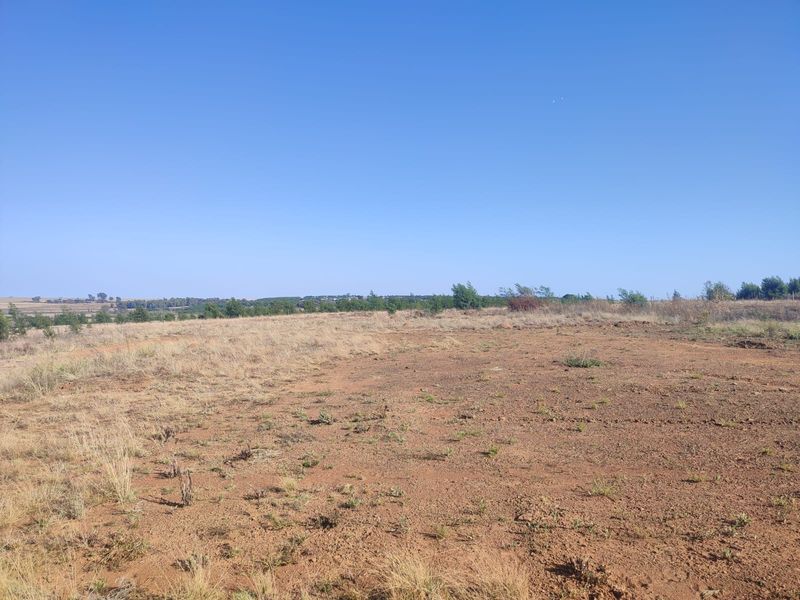 A wide-angle view of a vacant residential plot featuring natural terrain and open space, suitable for future development.