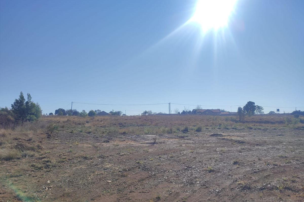 A wide-angle view of a vacant residential plot of land with natural vegetation and overhead power lines visible in the distance.