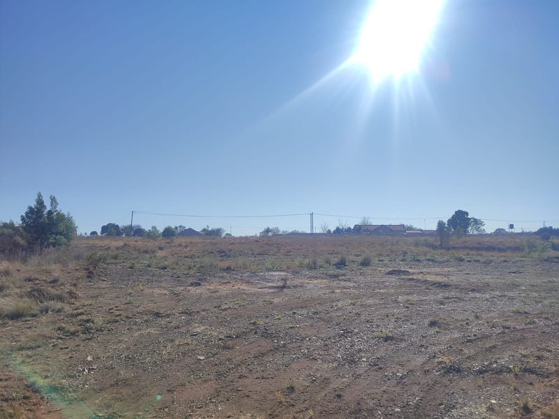 A wide-angle view of a vacant residential plot of land with natural vegetation and overhead power lines visible in the distance.