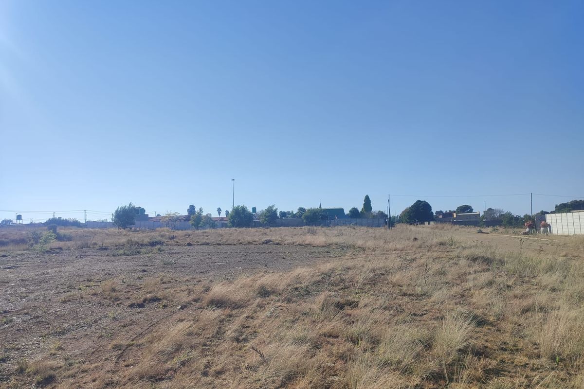 A wide-angle view of a vacant residential plot featuring dry grass and boundary fencing, suitable for future development.