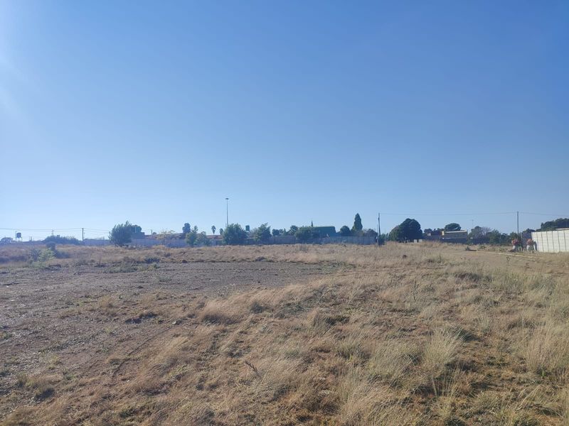 A wide-angle view of a vacant residential plot featuring dry grass and boundary fencing, suitable for future development.