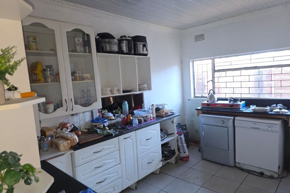 A functional kitchen featuring white built-in cabinetry, tiled flooring, and a window with security bars, offering a practical layout for daily meal preparation.