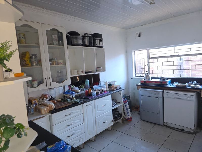 A functional kitchen featuring white built-in cabinetry, tiled flooring, and a window with security bars, offering a practical layout for daily meal preparation.