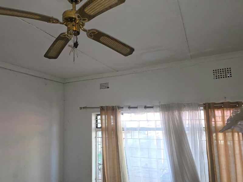 A bedroom featuring a ceiling fan with exposed wiring, security bars on the window, and visible water staining on the ceiling.
