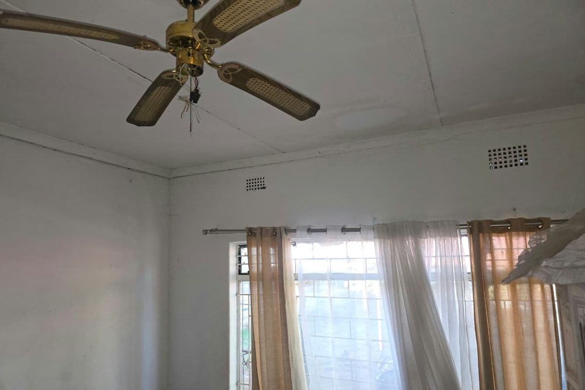 A bedroom featuring a ceiling fan with exposed wiring, security bars on the window, and visible water staining on the ceiling.