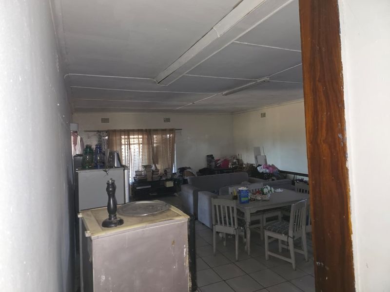 An open-plan living and dining area featuring tiled flooring and fluorescent lighting, requiring cosmetic updates to improve the overall condition and appeal.