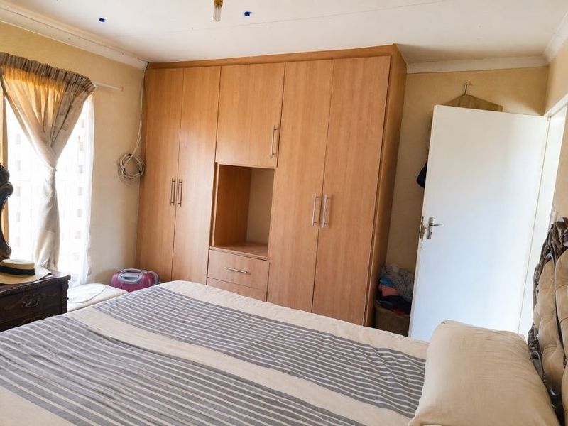 A bedroom featuring a large built-in wooden wardrobe, standard door, and window with curtains. The room requires minor cosmetic repairs to the ceiling.