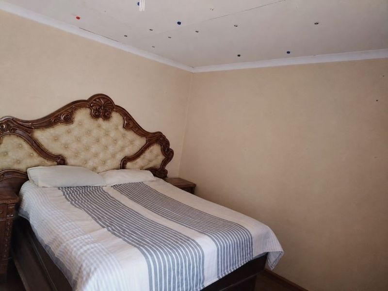A bedroom featuring plain walls and a ceiling with visible surface imperfections.
